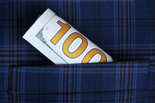 Rolled hundred dollar bill sticking out of a dark blue plaid fabric pocket, symbolizing finance, savings, and wealth.