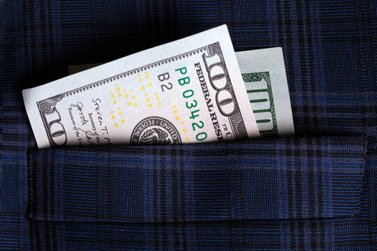 Closeup of a $100 US dollar bill tucked into a blue plaid suit pocket, symbolizing finance, success, and wealth.