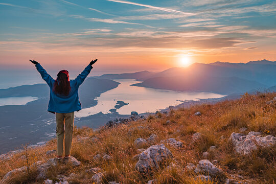 Woman with outstretched arms watching panoramic sunset over Bay of Kotor, embracing freedom, adventure in Montenegro