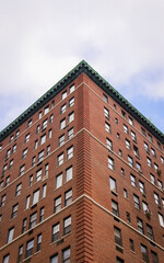 Fototapeta premium Manhattan red brick building. Low angle view of classic NYC apartment architecture with green cornice against sky.
