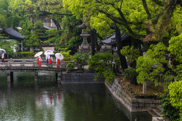 Fototapeta premium cuatro sacerdotisas japonesas bikshuni con su sombrilla tradicional sobre un puente de piedra en un dia lluvioso en osaka