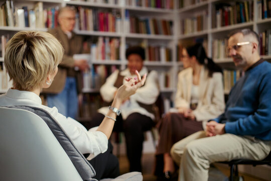 Middle aged woman leading group discussion with diverse adults during counseling session, back view. Useful for mental health, therapy, support group, communication campaigns