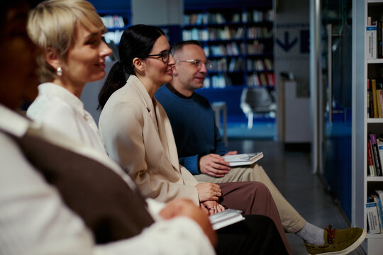 Multiethnic adults sitting in library, listening and discussing during group session, representing education and teamwork. Useful for training, workshop, community learning promotion