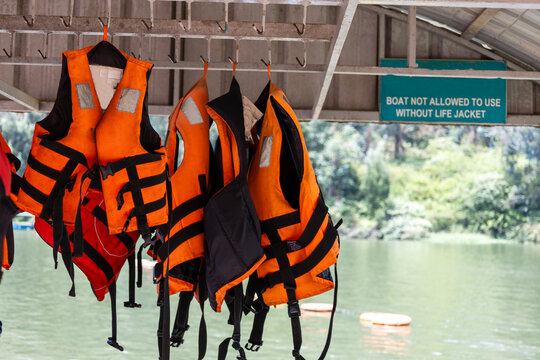 Orange life jackets hanging at a boat dock with a safety sign in the background. Ideal for water safety, boating, tourism, travel, emergency preparedness, rescue, and outdoor recreation concepts.