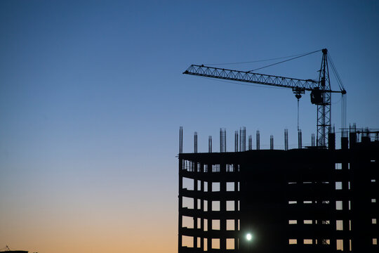 Silhouette of a building under construction with cranes at sunset