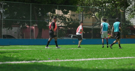 Fototapeta premium Group of friends enjoying casual soccer match on local field, players in colored vests running and passing ball, concept of teamwork, energy, and social recreation