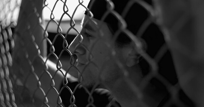 Hispanic man behind fence lost in ruminating thoughts, reflecting on past mistakes and inner struggle in black and white portrait