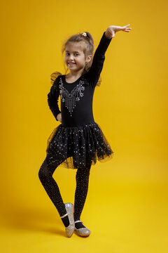 Smiling little girl in black dance costume posing on yellow background. Child portrait for dance, fashion and education.
