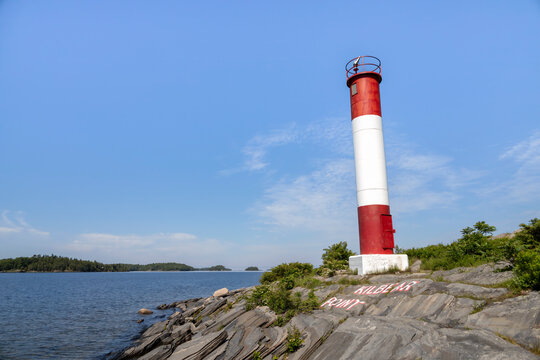 A vibrant red and white lighthouse stands on rocky shores at Killbear Provincial Park, Ontario, under a clear blue sky.