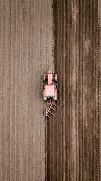 Overhead view of a red tractor plowing dark furrows across a cultivated field