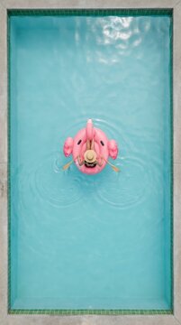 Overhead view of woman relaxing on a pink flamingo float in a turquoise pool