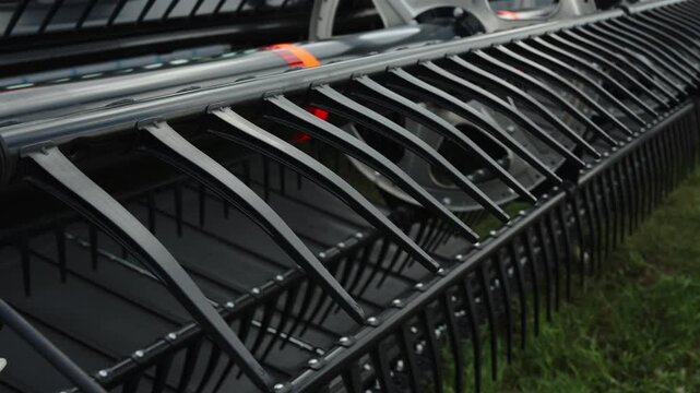A close-up shot captures the rows of glossy black plastic tines on a modern agricultural harvester reel.
