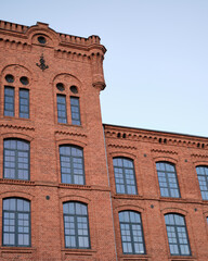 Obraz premium Decorative red brick facade with arched windows and ornate masonry, framed against clear sky with generous copy space for architecture and design projects.