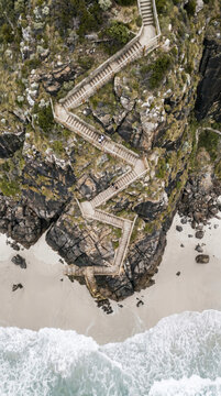 Aerial abstraction of a zigzag staircase descending a rocky cliff to the beach