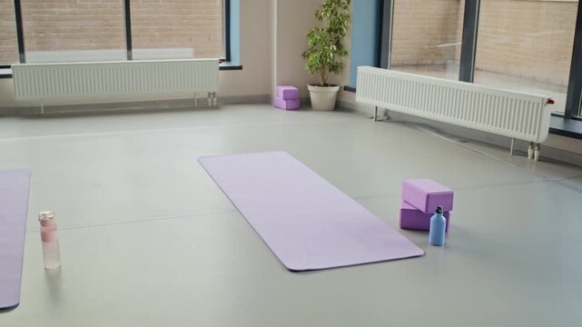 Yoga mats, blocks, and water bottles lying on floor in empty studio, camera panning to reveal spacious setup. Clip suited for promoting wellness centers, fitness apps, or mindfulness classes