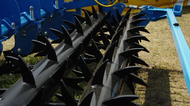 A close-up shot focuses on the black tined packer or spiked rollers of a modern agricultural soil tillage implement.