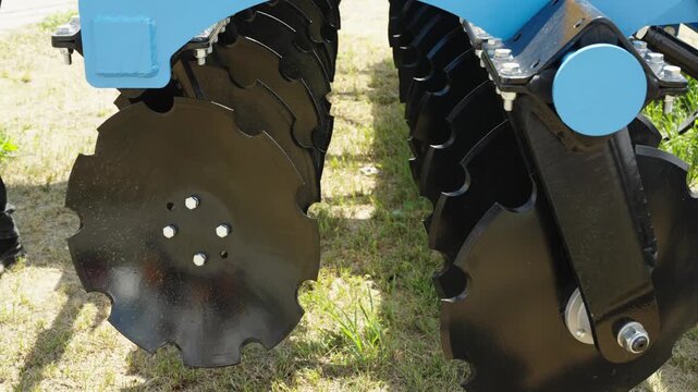 A close-up shot focuses on the sharp notched black discs of a modern agricultural disc harrow implement.