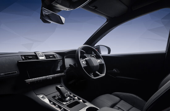 Right-hand drive luxury car interior with black leather. Car cockpit wide angle view from passenger side: seats, steering wheel, dashboard and center console.