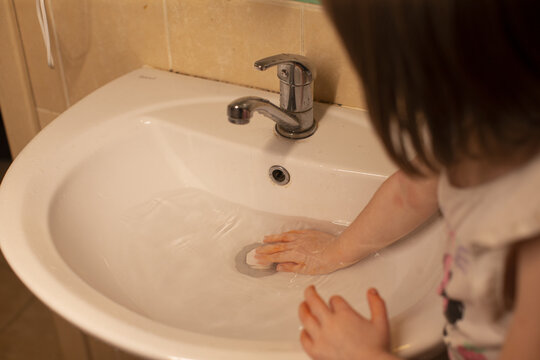Child washing hands with soapy cloth at sink, visible lather and careful rubbing of palms and fingers, domestic bathroom setting