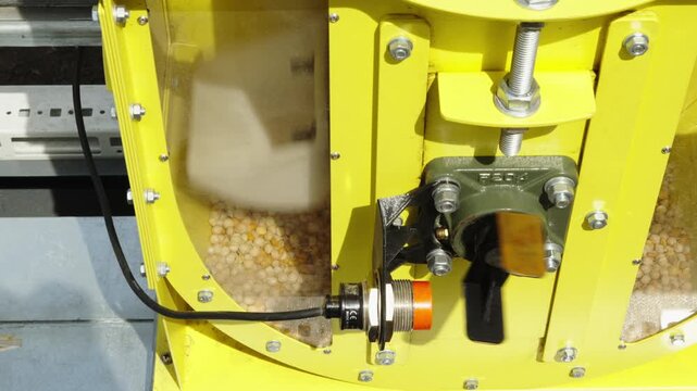 A close-up shot shows a capacitive proximity sensor with a red cap mounted near a rotating shaft bearing on a yellow agricultural machine with a grain inspection window.