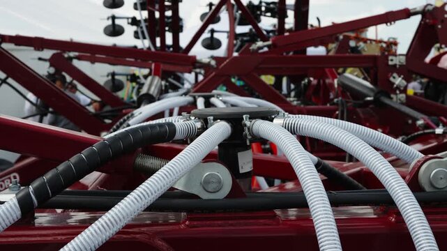 A close-up shot shows a central distribution head with white flexible seed tubes on a red agricultural planter.