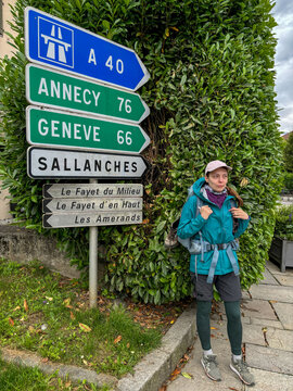 Woman stands beside French road signs to Annecy and Geneva