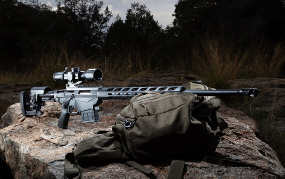 Precison rifle and backpack on a boulder when the sun is low on the horizon