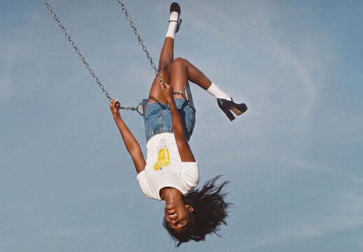 Mockup of T-shirt. Woman swings high in the air at a playground on a sunny day.