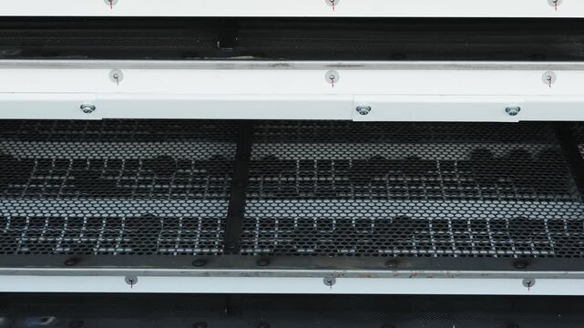 A close-up shot shows multiple layers of industrial metal screens or sieves in a grain cleaning machine.