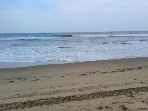 Scenic coastal view of ocean waves hitting a sandy beach with tire treads seascape landscape daylight vacation receding tranquil textured granules shoreline spindrift refreshing