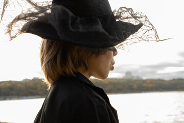 child's Halloween costume. A profile portrait of a child with their eyes hidden beneath a black witch's hat. Lips whispering trick or treat © Anna