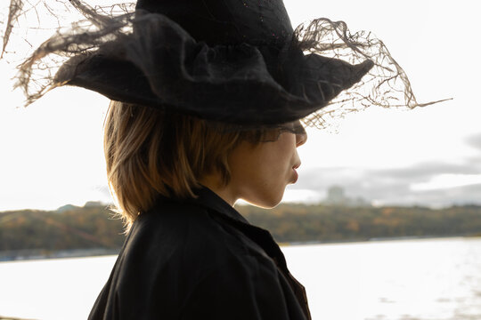 child's Halloween costume. A profile portrait of a child with their eyes hidden beneath a black witch's hat. Lips whispering trick or treat
