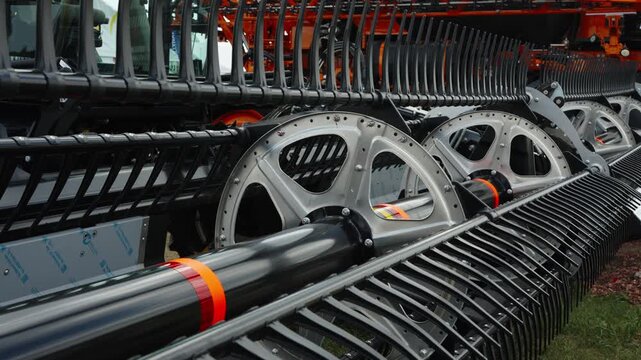 A close-up shot shows the shiny metal reel and black plastic tines of a modern agricultural combine harvester header.