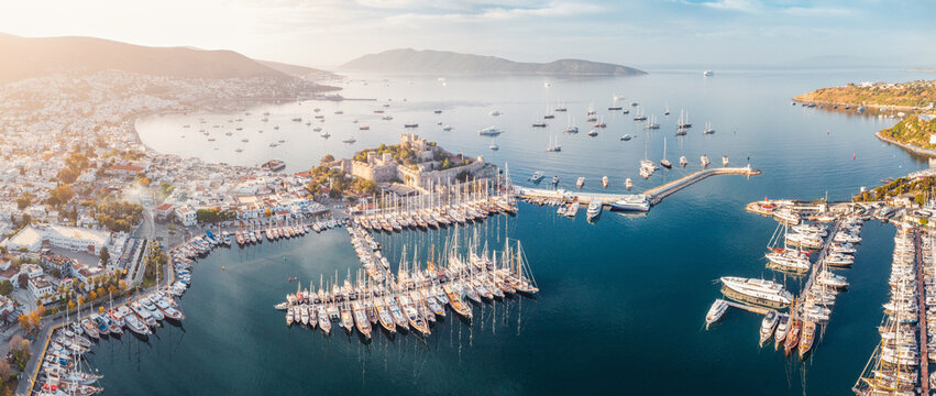 Aegean Sea harbor with Bodrum Castle, a busy marina filled with sailboats and a coastal town nestled by mountains on a sunny day