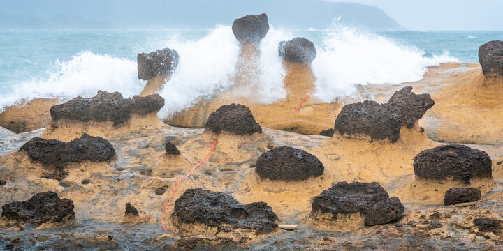 Scenic view of hoodoo stones rock formation with wave crashing on rocks in Yehliu geopark in New Taipei Taiwan