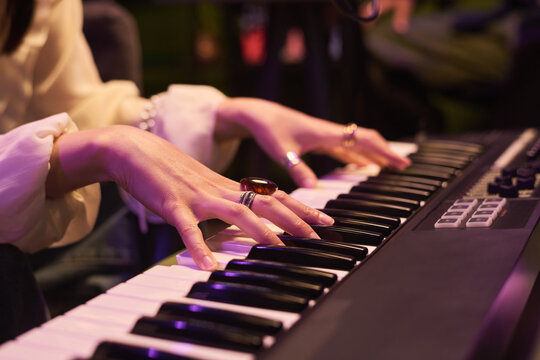 Close up of young womans hands playing digital keyboard during music performance, expressing creativity and entertainment. Ideal for music education, events, audio branding