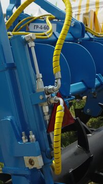 A hydraulic cylinder with yellow protective spiral wrap mounted on blue agricultural machinery with the label "ГР-4-60".