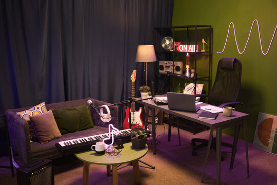 Wide shot of home podcast studio featuring laptop, microphone, keyboard, guitar, on air sign, supporting content creation, music production, streaming or remote media branding