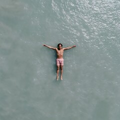 Fototapeta premium Aerial view of a man floating on calm turquoise water in pink swim shorts for summer relaxation background and wellness banner