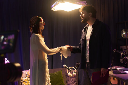 Young man and woman greeting and shaking hands in podcast studio, discussing media collaboration and content production. Useful for creator partnership or interview marketing