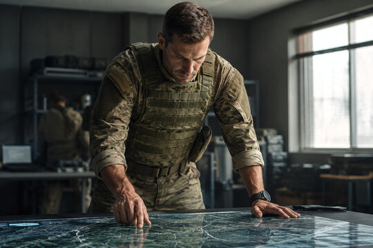 Military Soldier in Tactical Vest Pointing at Digital Map in Command Center. Concept of Military Strategy, Mission Planning, Leadership, and Situational Awareness during Briefing Session.
