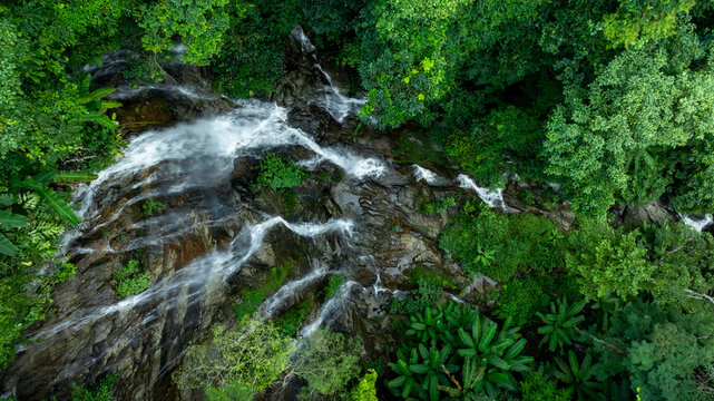 Aerial view of deep tropical rainforest with waterfall surrounded by lush tropical forest and towering cliffs streams of water into deep canyon, Lush green trees in forest with natural stream.