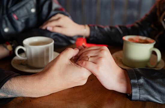 Pareja tomada de las manos durante una cita rom&aacute;ntica en una cafeter&iacute;a con tazas de caf&eacute; y ambiente acogedor