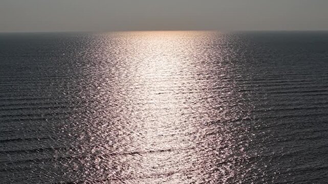 Golden sunlight reflects off the calm ocean water surface, creating a serene and tranquil atmosphere over the gently rippling sea