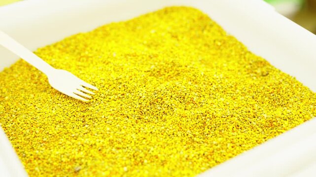 A white container filled with a large amount of bright yellow bee pollen granules with a wooden fork.