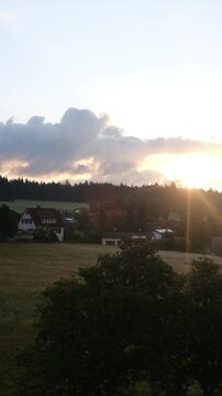 Golden sunset shining over a tranquil german countryside village with traditional houses nestled among lush green fields, forests, and rolling hills creating a serene landscape