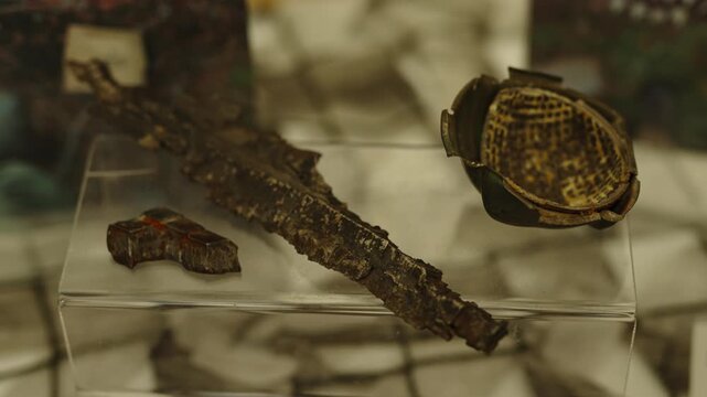 Ancient rusted iron artifacts, including a dagger or sword fragment and a small bowl, are displayed on a clear stand.