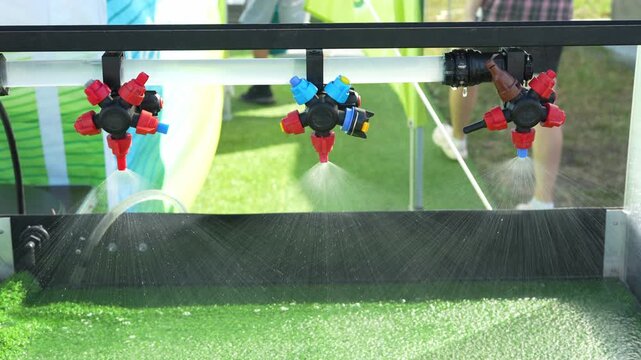 Three agricultural sprayer multi-nozzle bodies are spraying a fine water mist on a demonstration display.