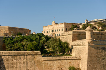 Fototapeta premium Vistas de la Auberge de Castille en La Valeta, Malta, desde los Upper Barrakka Gardens, que muestran la arquitectura de piedra caliza y las murallas de fortificación circundantes.