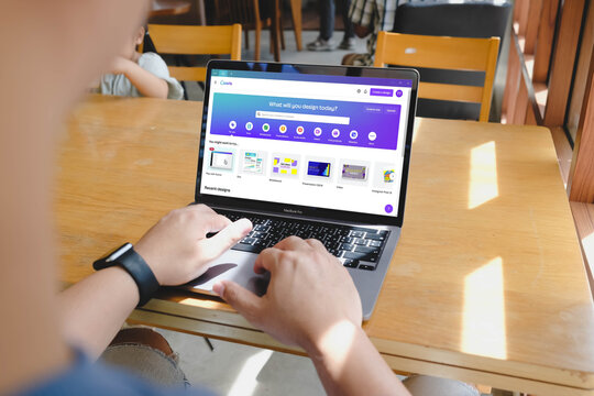 Bangkok, Thailand. July 12, 2026; An over the shoulder view of a person using a MacBook Pro laptop to design on the Canva web application platform in a cafe.